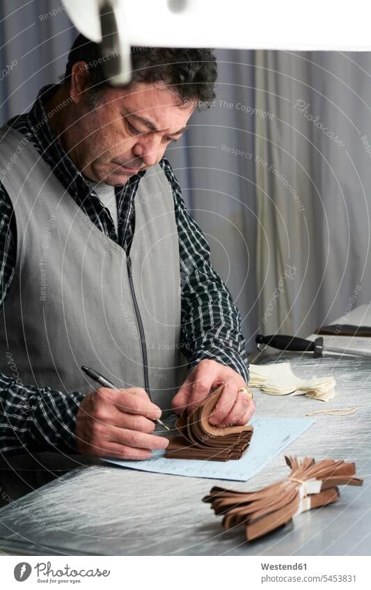 Schuhmacher betrachtet Muster in seiner Werkstatt arbeiten Arbeit Schuster Handwerker Handwerksberuf Handwerksberufe Gewerbe Werkstätte Werkstaette Werkstaetten