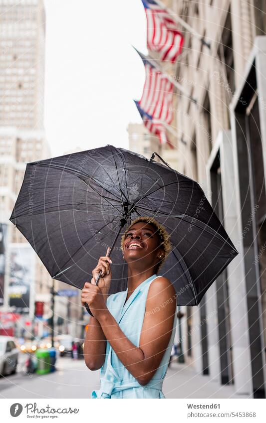 USA, New York, junge blonde afro-amerikanische Frau mit Regenschirm regnen weiblich Frauen lächeln Freude freuen Regenschirme Afroamerikanisch Afro-Amerikanisch