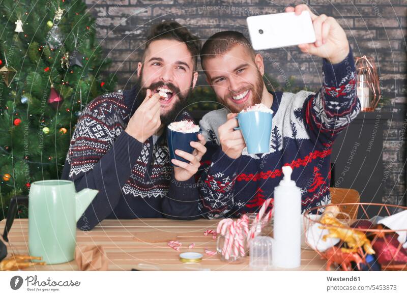 Glückliches homosexuelles Paar, das ein Selfie mit dem Smartphone zu Weihnachten zu Hause macht Selfies Portrait Porträts Portraits Schwules Paar Schwuler