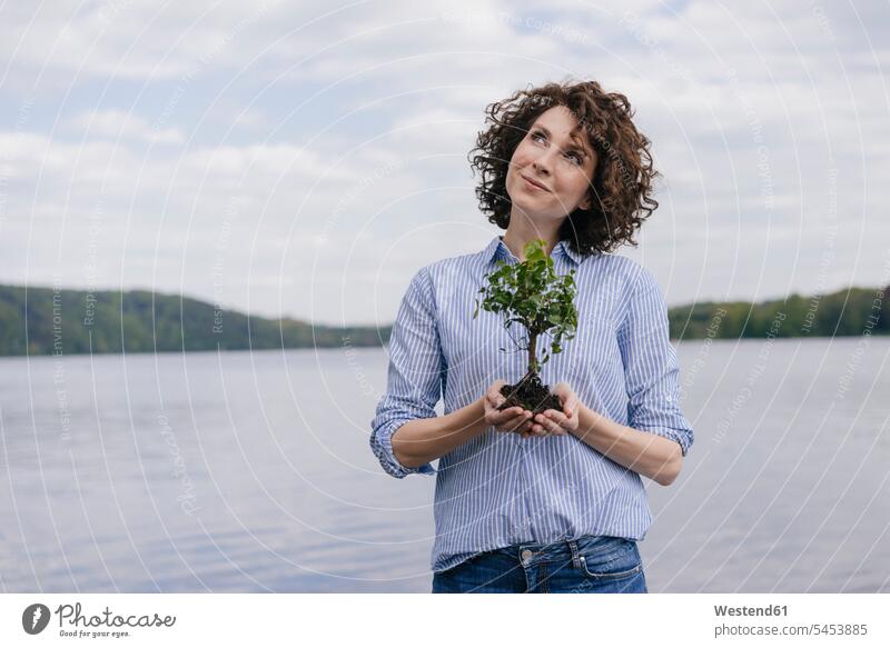 Frau am See hält Bäumchen in der Hand Naturschutz weiblich Frauen Baum Bäume Baeume Seen Ökologie Umwelt- und Naturschutz Umweltthemen Erwachsener erwachsen