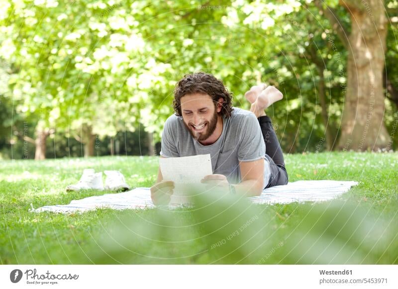 Lachender Mann liegt auf einer Decke in einem Park und liest einen Brief Männer männlich Briefe Erwachsener erwachsen Mensch Menschen Leute People Personen Post