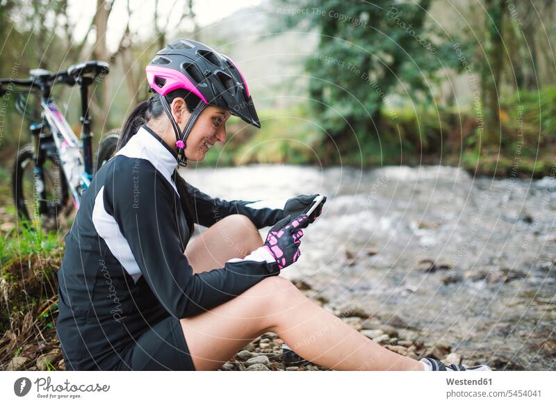 Lächelnde Frau mit Mountainbike, die sich in der Natur ausruht und ihr Handy überprüft weiblich Frauen Mountainbikes Mobiltelefon Handies Handys Mobiltelefone