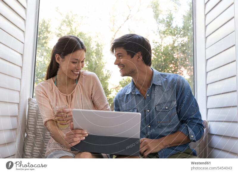 Lächelndes junges Paar sitzt auf der Fensterbank und teilt sich ein Tablett Pärchen Paare Partnerschaft entspannt entspanntheit relaxt Tablet Computer Tablet-PC
