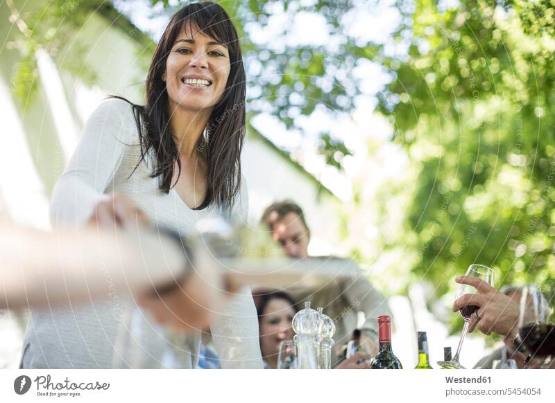Lächelnde Frau beim Familienessen im Garten Gruppe Gruppe von Menschen Menschengruppe Wein Weine servieren Rotwein Rotweine feiern lächeln Freunde Leute People