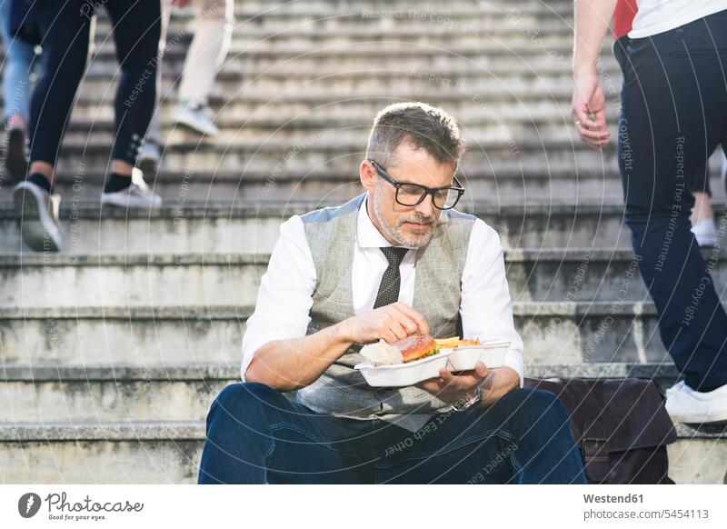 Geschäftsmann in der Stadt sitzt auf einer Treppe und isst einen Hamburger Businessmann Businessmänner Geschäftsmänner Treppenaufgang Pause Geschäftsleute