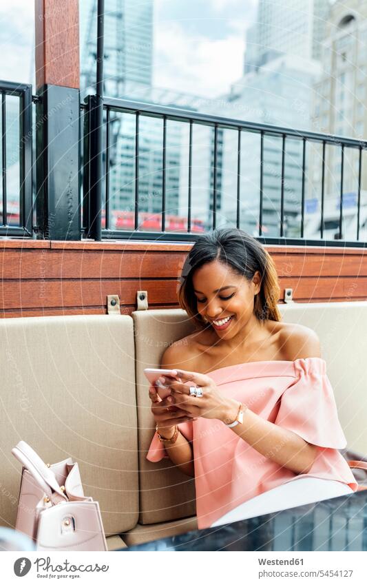 Lächelnde Frau, die in der Stadt mit ihrem Smartphone Nachrichten verschickt Handy Mobiltelefon Handies Handys Mobiltelefone lächeln weiblich Frauen Telefon