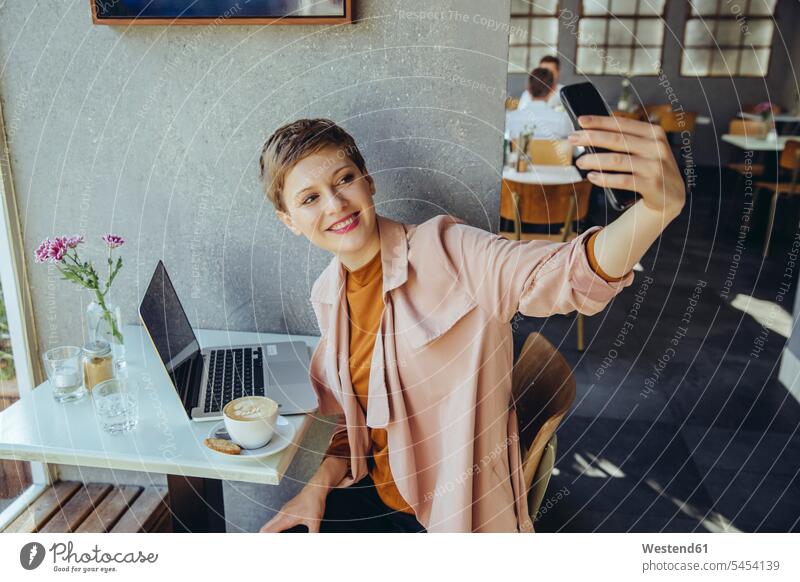 Frau macht ein Selfie mit Kaffee und Laptop in einem Cafe lächeln weiblich Frauen Notebook Laptops Notebooks Selfies Kaffeehaus Bistro Cafes Café Cafés