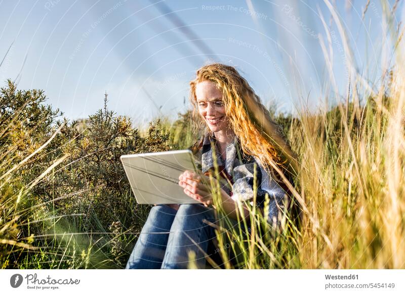Niederlande, Zandvoort, lächelnde Frau mit Tablette in den Dünen sitzend Tablet Computer Tablet-PC Tablet PC iPad Tablet-Computer Sanddüne Sanddünen Strand