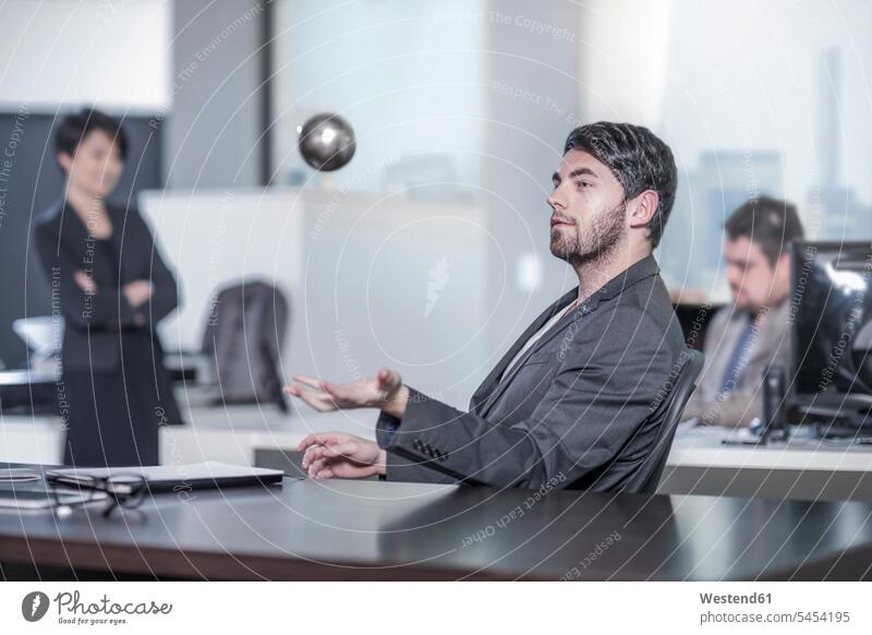 Mann sitzt am Schreibtisch im Stadtbüro und wirft einen Ball in die Luft Männer männlich Bälle Büro Office Büros werfen Wurf Erwachsener erwachsen Mensch