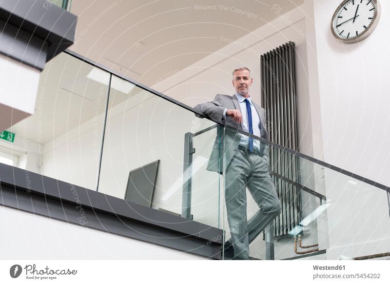 Reifer Geschäftsmann steht am Geländer in seinem Büro Businessmann Businessmänner Geschäftsmänner stehen stehend Office Büros Erfolg Erfolge erfolgreich modern