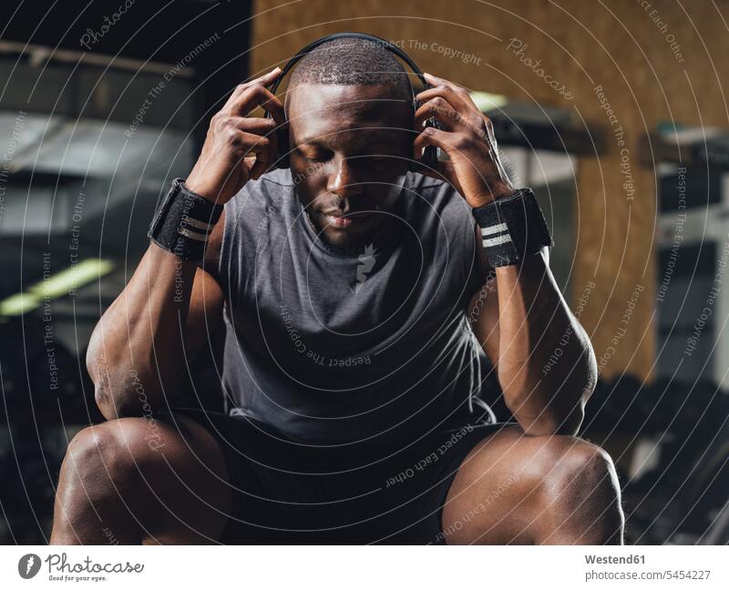 Athlet sitzt im Fitnessstudio, trägt Kopfhörer, konzentriert sich Kopfhoerer Muskeln muskulös athletisch Fitnessclubs Fitnessstudios Turnhalle Sportler