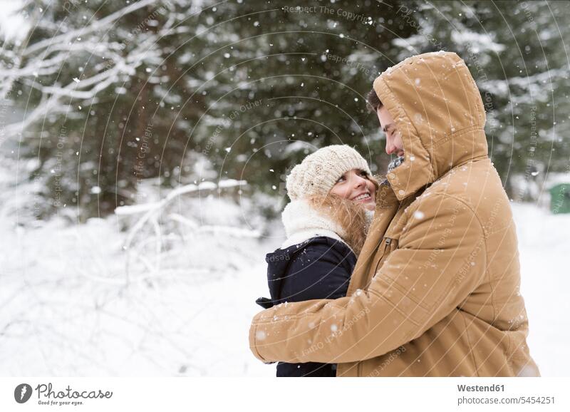 Glückliches junges Paar steht sich im schneebedeckten Winterwald gegenüber Pärchen Paare Partnerschaft Mensch Menschen Leute People Personen glücklich
