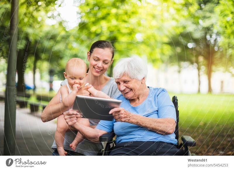 Grossmutter, Tochter und Enkelin amüsieren sich in einem Park mit Tabletten Parkanlagen Parks Großmutter Oma Grossmama Großmütter Omi Spaß Spass Späße spassig