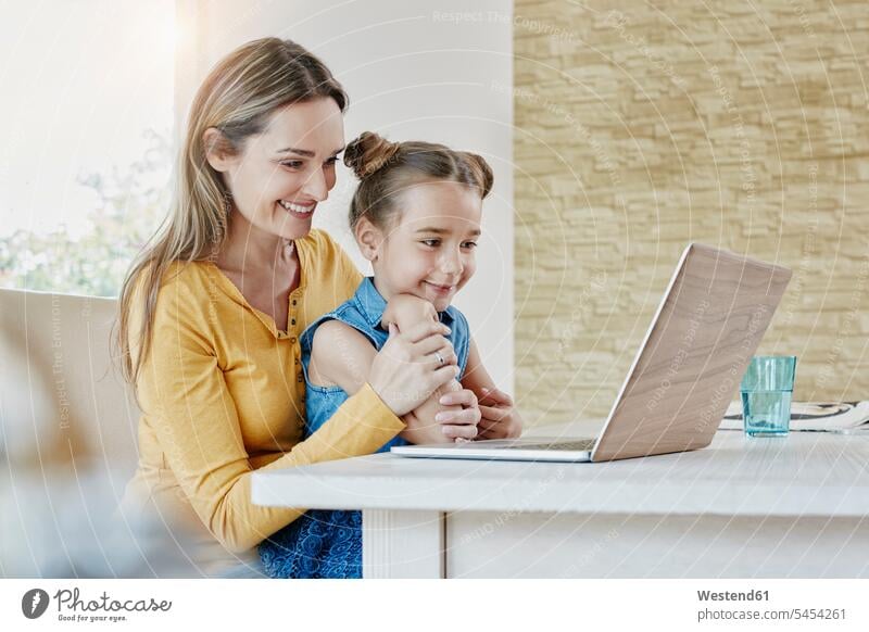 Glückliche Mutter mit Tochter zu Hause, die auf den Laptop schaut Mami Mutti Mütter Mama Internet Notebook Laptops Notebooks Töchter ansehen lachen glücklich