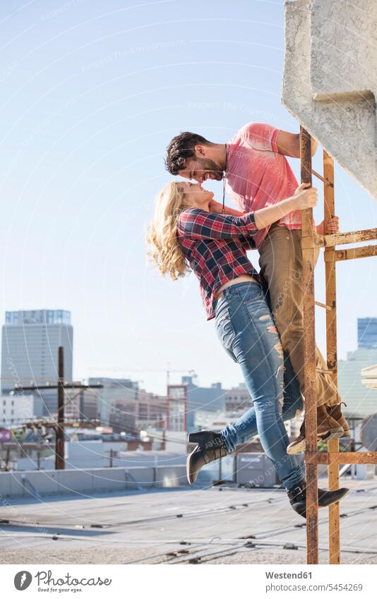 Junges Paar küsst sich auf einer Feuerleiter auf einem Dach verliebt glücklich Glück glücklich sein glücklichsein Pärchen Paare Partnerschaft küssen Küsse Kuss