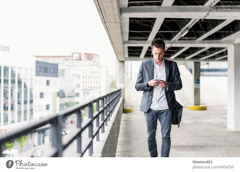 Junger Geschäftsmann mit Smartphone, zu Fuß auf Parkebene unterwegs auf Achse in Bewegung Urban städtisch Urbanität Urbanitaet iPhone Smartphones Anruf