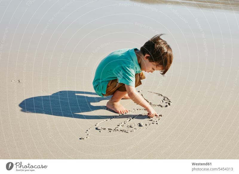 Kleiner Junge beim Zeichnen im Sand am Strand Buben Knabe Jungen Knaben männlich Beach Straende Strände Beaches ritzen kratzen Kind Kinder Kids Mensch Menschen