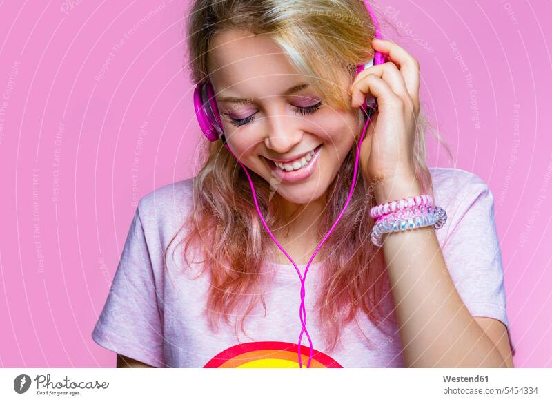Porträt einer jungen Frau, die mit Kopfhörern vor rosa Hintergrund Musik hört weiblich Frauen Kopfhoerer Portrait Porträts Portraits Erwachsener erwachsen