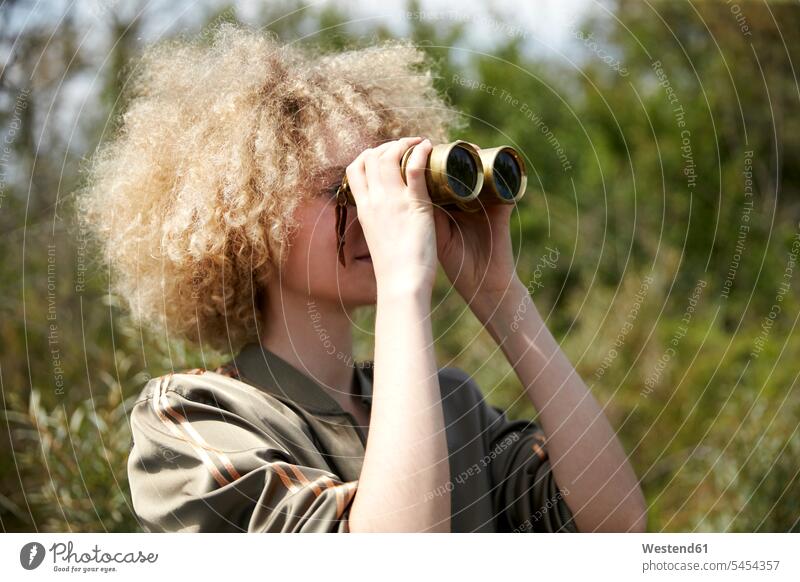 Junge Frau mit lockigem Haar schaut durch ein altes Fernglas Ferngläser Feldstecher Fernglaeser beobachten zuschauen ansehen weiblich Frauen Erwachsener