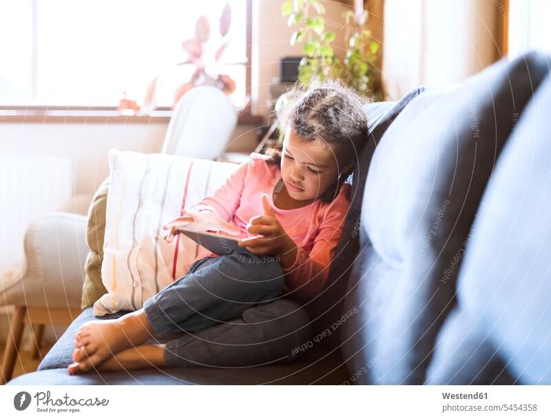 Kleines Mädchen am Sitztablett, auf dem Sofa sitzend Couches Liege Sofas weiblich Allein alleine einzeln Zuhause zu Hause daheim Tablet Tablet Computer