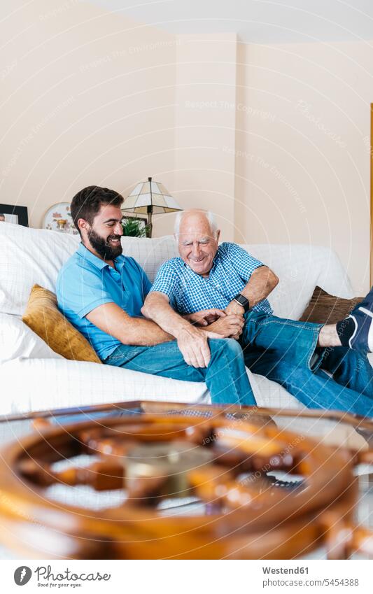 Der erwachsene Enkel und sein Großvater sitzen zu Hause auf der Couch und kitzeln sich gegenseitig Enkelsöhne Enkelsohn Opa Großpapa Großpapas Opas Opi