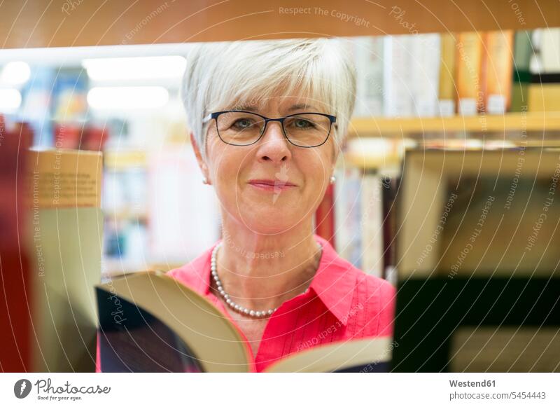 Porträt einer lächelnden älteren Frau mit Buch in einer Stadtbibliothek Bücher Portrait Porträts Portraits Bibliothek Gebäude Bauwerk Bauwerke Seniorin