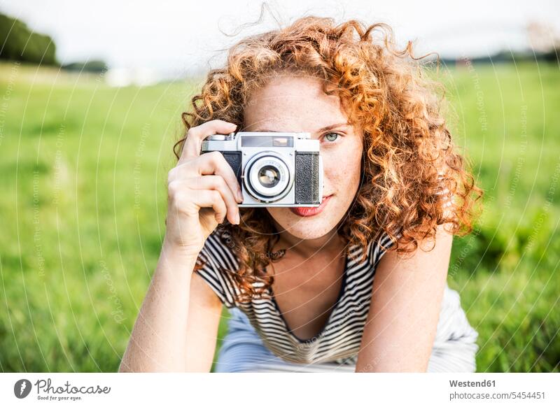 Junge Frau auf einer Wiese, die einen Betrachter mit der Kamera fotografiert fotografieren Portrait Porträts Portraits weiblich Frauen Erwachsener erwachsen