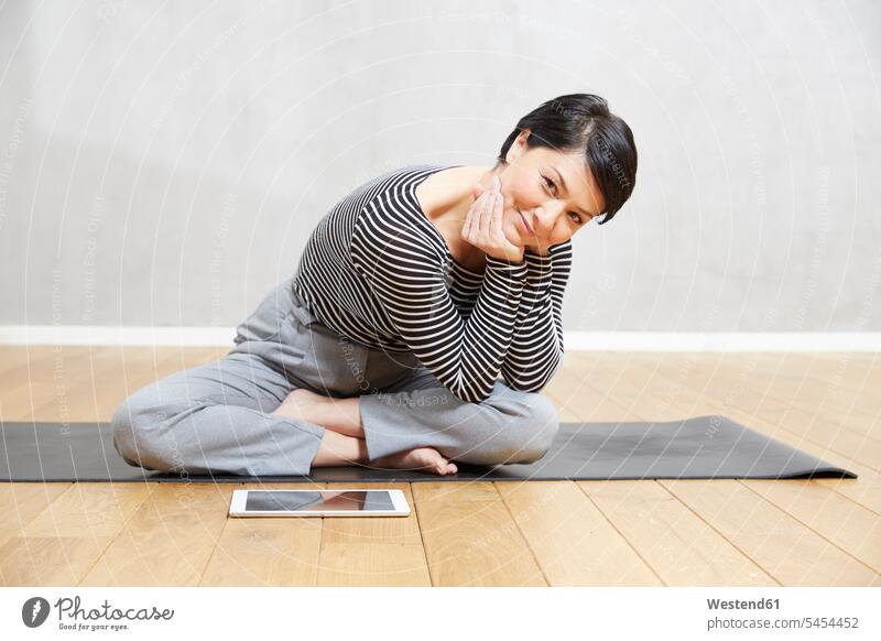 Lächelnde Frau sitzt auf Yogamatte mit Tablette Übung Uebung Übungen Uebungen sitzen sitzend Tablet Computer Tablet-PC Tablet PC iPad Tablet-Computer weiblich