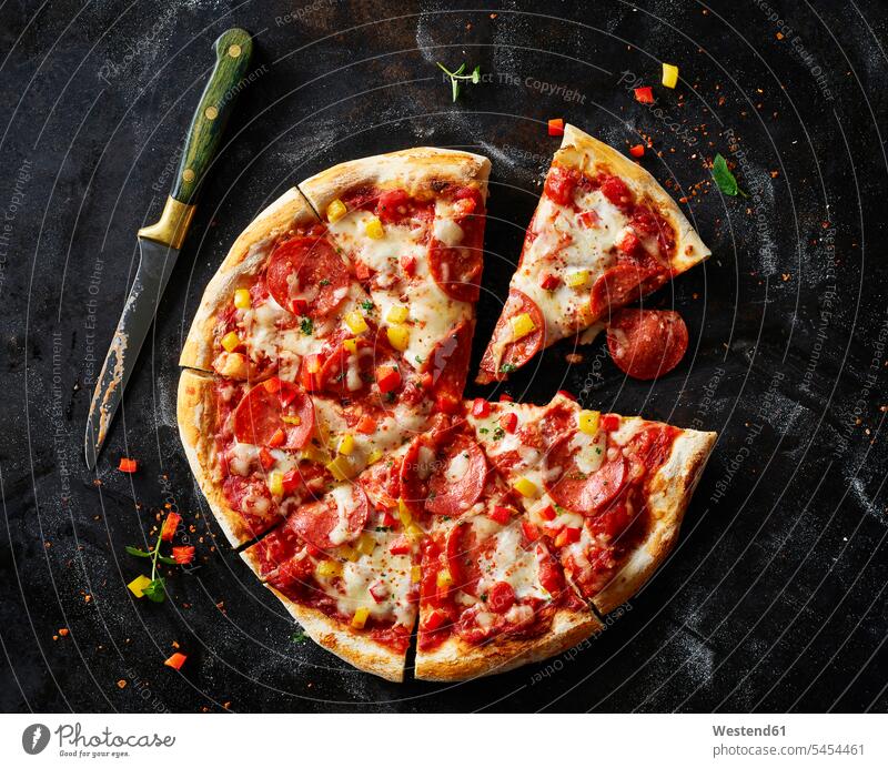 Aufgeschnittene Pizza mit Salami auf dunklem Boden Food and Drink Lebensmittel Essen und Trinken Nahrungsmittel rote Paprika selbstgemacht selbstgemachte