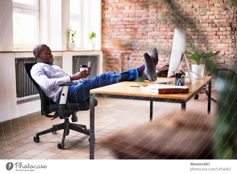 Geschäftsmann sitzt im Büro mit den Füßen auf dem Schreibtisch und prüft Handy sitzen sitzend Mobiltelefon Handies Handys Mobiltelefone Office Büros
