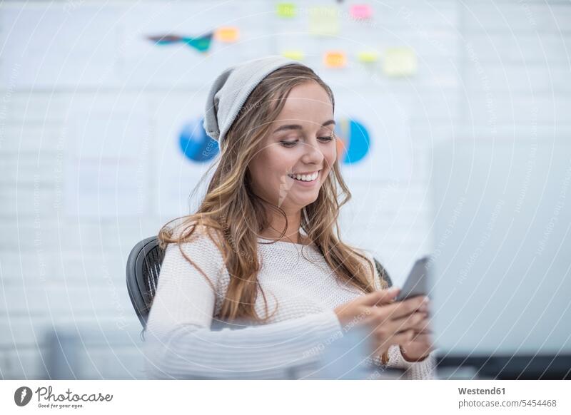 Junge Frau, die im Büro arbeitet und Textnachrichten liest Schreibtisch Arbeitstisch Schreibtische sitzen sitzend sitzt arbeiten Büroangestellte glücklich Glück