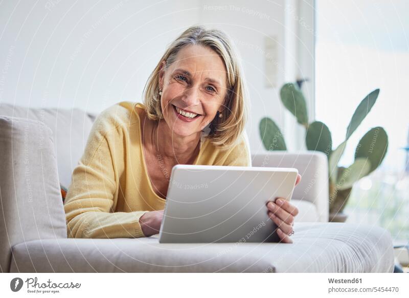 Lächelnde reife Frau zu Hause mit Tablette auf dem Sofa Tablet Computer Tablet-PC Tablet PC iPad Tablet-Computer liegen liegend liegt lächeln Couches Liege