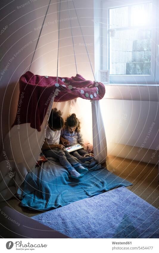 Zwei Schwestern sitzen im dunklen Kinderzimmer und schauen auf ein digitales Tablet spielen lesen Lektüre dunkel sitzend sitzt Zimmer Raum Räume Geschwister