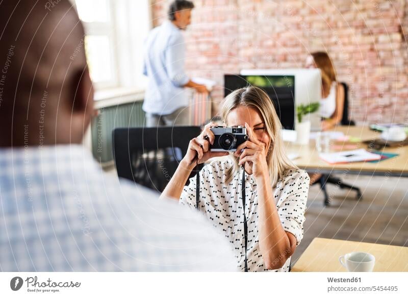 Geschäftsfrau mit Kamera, die einen Kollegen im Büro fotografiert Fotoapparat Fotokamera Office Büros fotografieren Arbeitskollegen Geschäftsfrauen