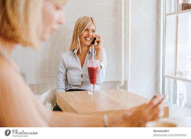 Junge Frauen am Handy in einem Cafe Kaffeehaus Bistro Cafes Café Cafés Kaffeehäuser Smoothie Smoothies Mobiltelefon Handies Handys Mobiltelefone lächeln