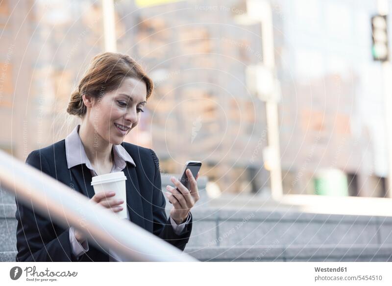 Lächelnde Geschäftsfrau hält Handy und Kaffee zum Mitnehmen Geschäftsfrauen Businesswomen Businessfrauen Businesswoman Geschäftsleute Geschäftspersonen