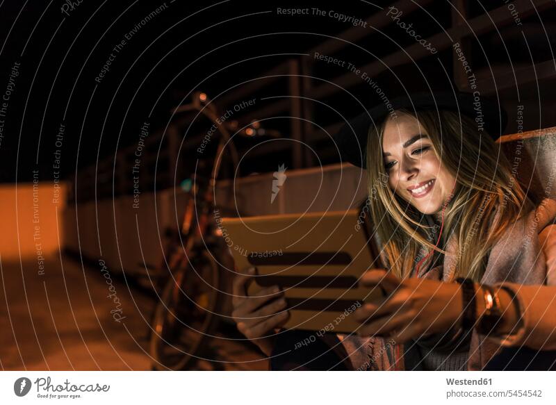 Lächelnde junge Frau in der Stadt, die nachts Tabletten nimmt lächeln Ohrhörer weiblich Frauen Tablet Computer Tablet-PC Tablet PC iPad Tablet-Computer