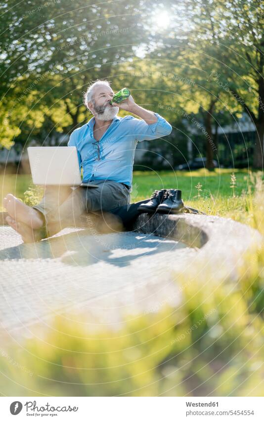 Reifer Mann trinkt Bier und benutzt Laptop im Park Wiese Wiesen sitzen sitzend sitzt Notebook Laptops Notebooks Männer männlich trinken Computer Rechner