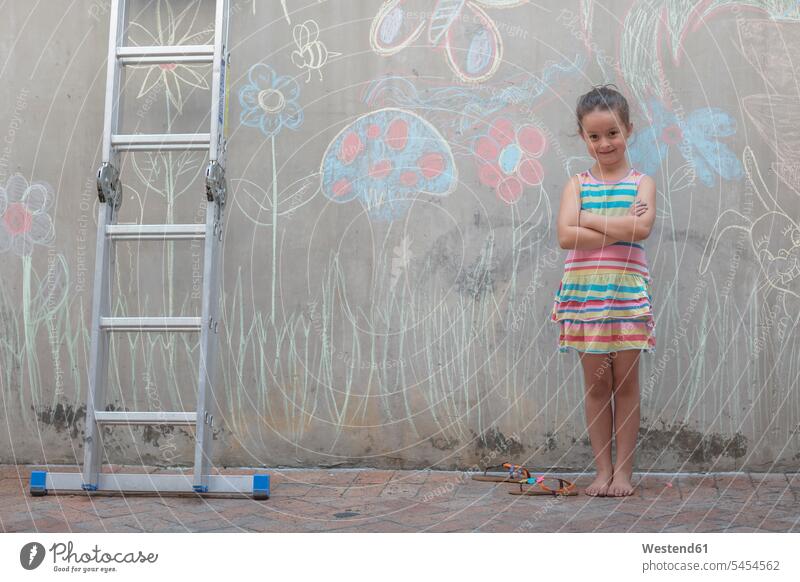 Mädchen steht neben bunten Bildern an einer Betonwand stehen stehend Betonwände Betonwaende weiblich farbig mehrfarbig zeichnen Zeichnung Wand Wände Waende Kind