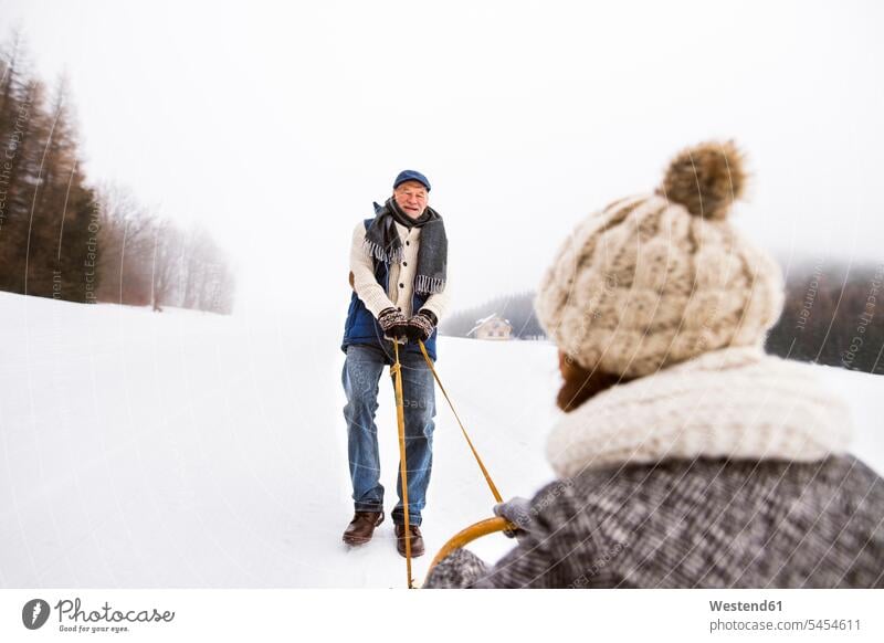 Glückliches Seniorenpaar amüsiert sich mit Schlitten in verschneiter Landschaft ältere Männer älterer Mann Schnee männlich Erwachsener erwachsen Mensch Menschen