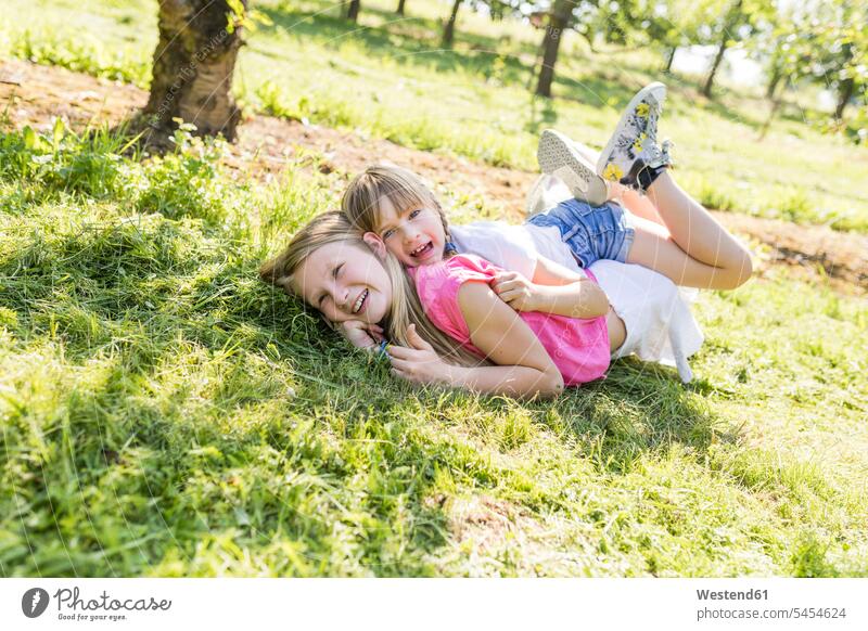 Zwei glückliche Schwestern spielen auf der Wiese Wiesen Glück glücklich sein glücklichsein liegen liegend liegt Garten Gärten Gaerten Mädchen weiblich