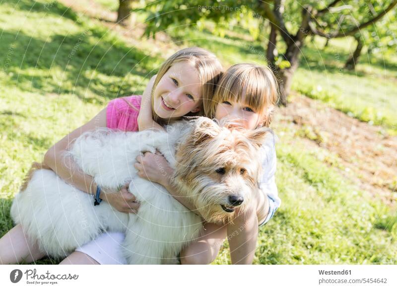Zwei lächelnde Schwestern kuscheln mit Hund auf der Wiese Wiesen Mädchen weiblich Hunde Garten Gärten Gaerten glücklich Glück glücklich sein glücklichsein Kind