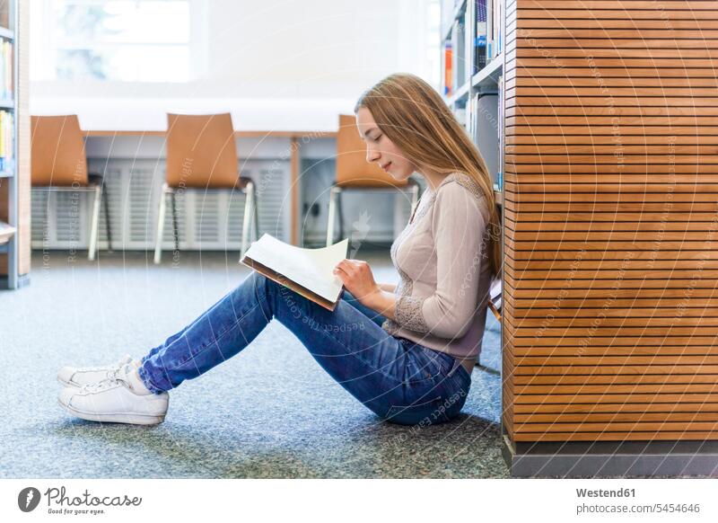 Teenagerin, die in einer öffentlichen Bibliothek auf dem Boden sitzt und ein Buch liest lesen Lektüre Bücher junges Mädchen Teenagerinnen weiblich junge Frau