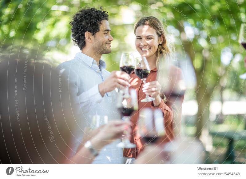 Ein Paar, das zusammen mit Wein im Garten anstößt Rotwein Rotweine Freunde feiern Gruppe Gruppe von Menschen Menschengruppe Weine Familie Familien Pärchen Paare