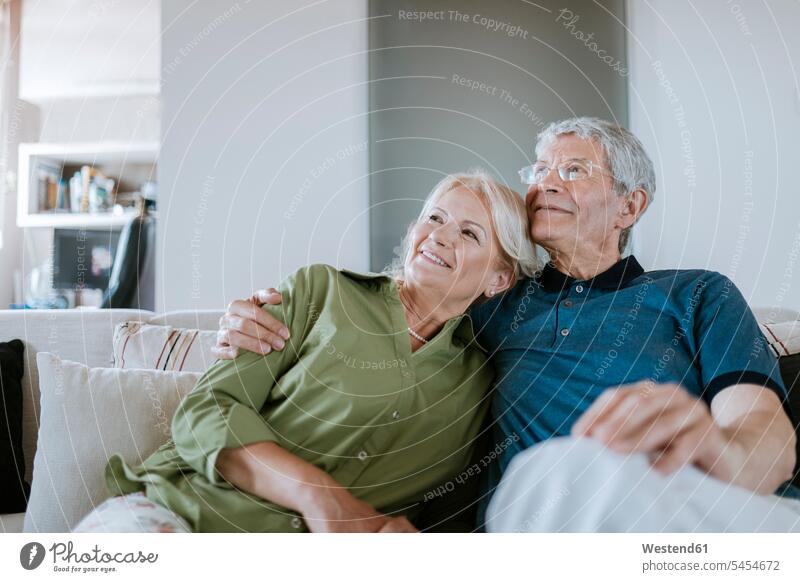 Lächelndes älteres Paar sitzt zu Hause auf der Couch lächeln Senior ältere Männer älterer Mann Senioren Pärchen Paare Partnerschaft Sofa Couches Liege Sofas