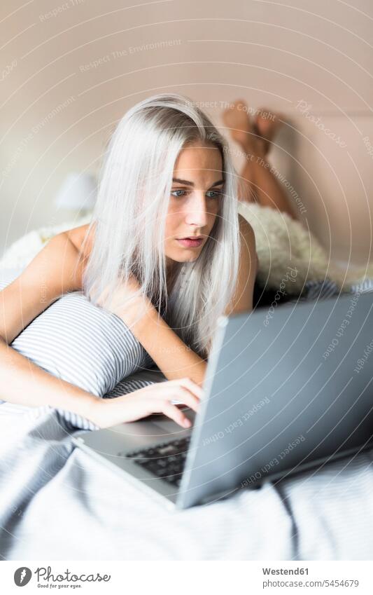 Junge Frau liegt mit Laptop im Bett liegen liegend Betten Notebook Laptops Notebooks weiblich Frauen Computer Rechner Erwachsener erwachsen Mensch Menschen