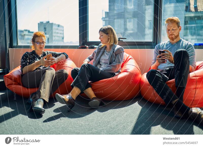 Kollegen mit Mobiltelefonen sitzen in Sitzsäcken in der Büro-Lounge Handy Handies Handys Office Büros Arbeitskollegen sitzend sitzt Lounges Sitzsack Telefon