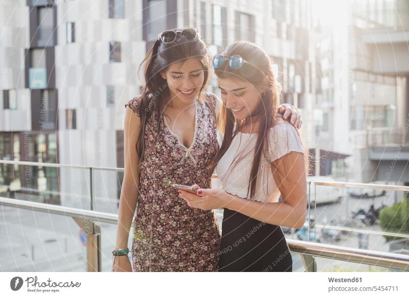 Zwei lächelnde junge Frauen beim Blick auf das Handy in der Stadt Mobiltelefon Handies Handys Mobiltelefone Freundinnen Telefon telefonieren Kommunikation