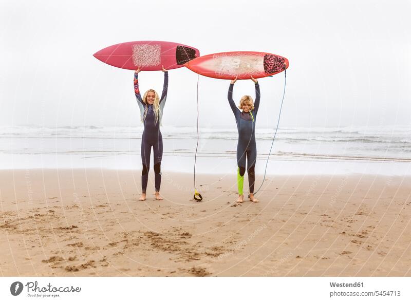 Spanien, Aviles, zwei junge Surfer am Strand mit ihren Surfbrettern Teenager Jugendliche Heranwachsende Pubertierende surfboard surfboards heben Wellenreiter