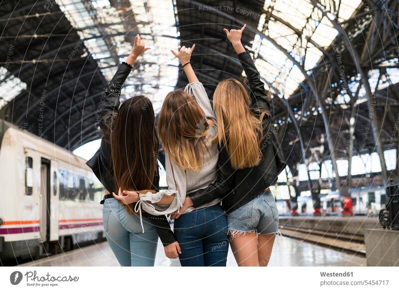 Rückenansicht von drei jungen Frauen, die Arm in Arm auf einer Plattform stehen Bahnsteig Zugbahnsteig Zugbahnsteige Bahnsteige Freundinnen Bahnhof Bahnhöfe